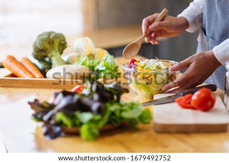 Closeup image of a female chef cooking and holding a bowl of fresh mixed vegetables salad in kitchen Royalty-Free Stock Photo #1679492752