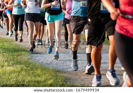 A straight line of runners racing on a dirt path in a State Park during a 5K community race. Royalty-Free Stock Photo #1679499934