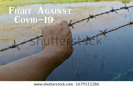 The hands of people holding barbed wire fence with the words " Fight Against Covid-19". Concept of Never give up for fighting virus