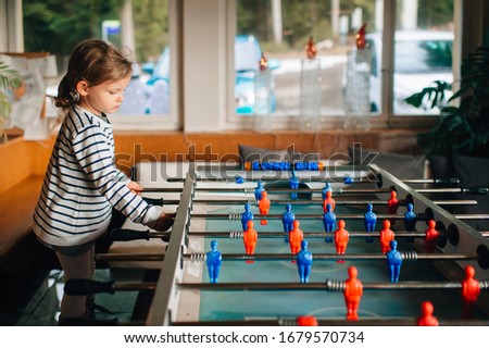 Picture of little beautiful girl with fair hair plays in a table hockey at home