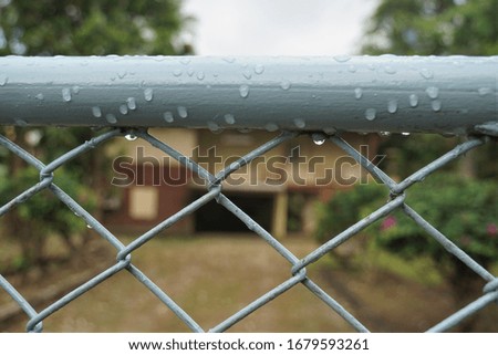 Wire mesh fence with water droplets and a blurry background of an ancient wooden house.