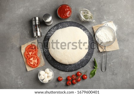 Flat lay composition with dough and fresh ingredients for pizza on grey table