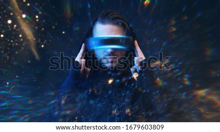 Young man in hoodie on virtual reality background. Guy using VR helmet. Augmented reality, future technology, game concept. Blue neon light. 