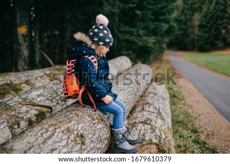 Picture of lovely young caucasian children with pretty face, big eyes in knitted hat goes for a walk in a forest