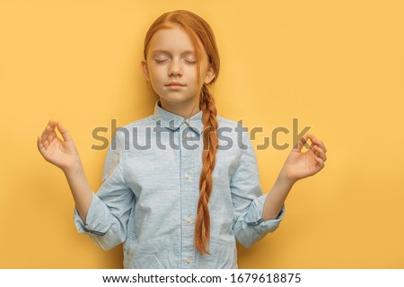 Yoga. portrait of calm relaxed caucasian red haired girl in casual wear, isolated over yellow background. child with freckles keep calm with closed eyes