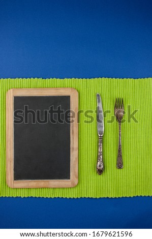 menu blackboard frame with knife and fork for recipes or menu on blue background with green tablecloth