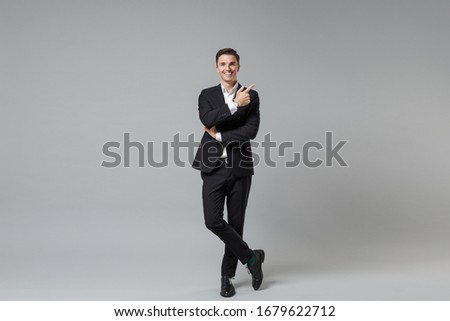 Smiling young business man in classic black suit shirt posing isolated on grey background studio portrait. Achievement career wealth business concept. Mock up copy space. Pointing index finger up Royalty-Free Stock Photo #1679622712