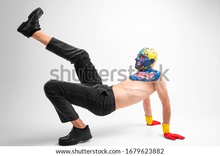 A strange man with makeup on his head and shoulder in red-yellow gloves, black pants and boots, no T-shirt dances