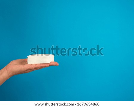 Hand with pile of tissues on blue background with copy space