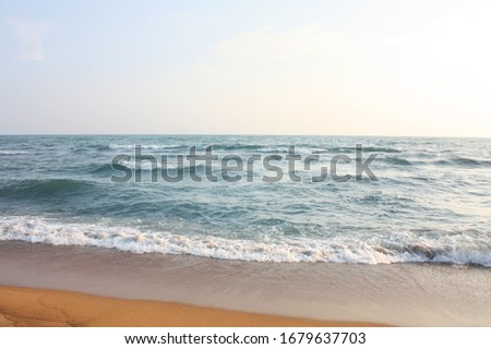 Beautiful side view of the ocean, sea, surf waves with sea foam. Empty sandy beach and water. Beautiful azure sea and cloudy sky