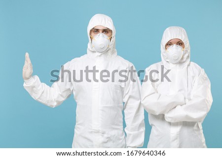 Two people in protective suits respirator masks isolated on blue background studio. Epidemic pandemic new rapidly spreading coronavirus 2019-ncov originating in Wuhan China virus concept stop gesture