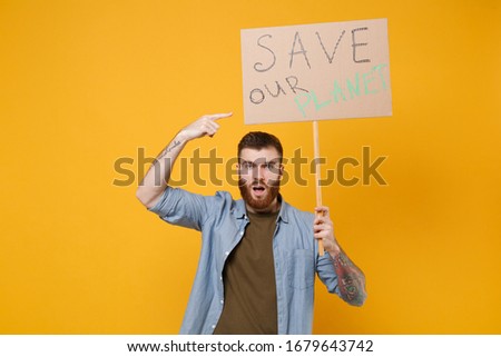 Nervous young protesting man pointing index finger on protest sign broadsheet placard on stick isolated on yellow background. Stop nature garbage ecology environment protection concept. Save planet