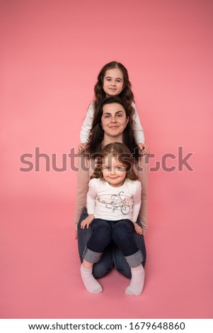 Portrait of charming beautiful friendly king supportive cute family members sitting one by one and looking at the camera, isolated over pink background