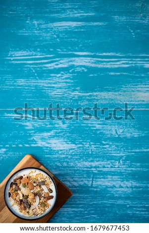 A bowl with yogurt and granola, on a blue background. There is a space on a picture for your information.