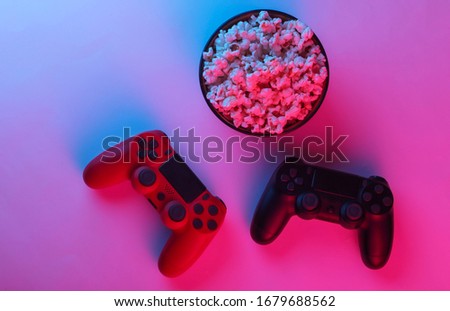 Two gamepads and a bowl of popcorn. Neon pink blue light. Gaming, leisure and entertainment concept. Top view