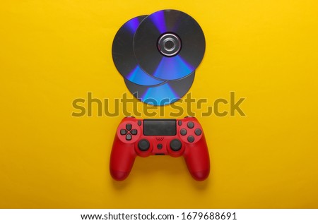 Red gamepad and cd compact discs on yellow background. Gaming, entertainment concept. Top view