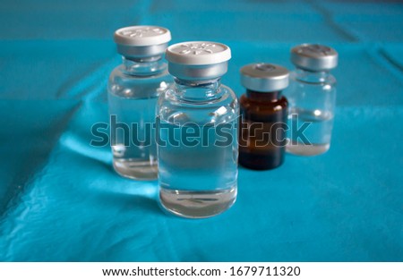 One transparent vial with injection solution and other vial in the background.