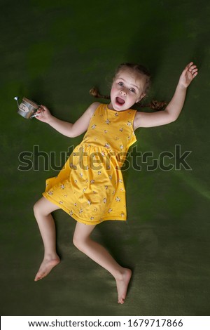 Girl in a yellow dress with a watering can in hand lies on a green background, spring mood