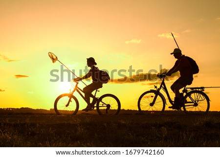Father and son returning from fishing in the evening, silhouettes of people riding bicycles in nature 