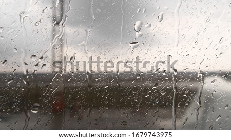 Water drops on the glass. Drops trickle down the window of the plane, rain on the runway. Flying on a plane in cloudy weather with precipitation. Template. Royalty-Free Stock Photo #1679743975