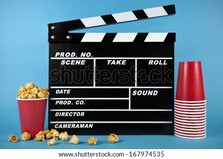 Clapperboard with popcorn and red glasses on blue background 