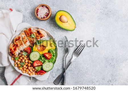 Healthy vegetable buddha bowl lunch with grilled chicken and chickpeas, cucumber, tomato and avocado on light gray background. Top view. Zero waste concept