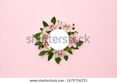 White round frame decorated with green leaves and orchid flowers on pink pastel background. empty space for text. mock up with copy space. Tropical nature. Flat lay