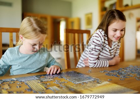 Cute young girls playing puzzles at home. Children connecting jigsaw puzzle pieces in a living room table. Kids assembling a jigsaw puzzle. Fun family leisure. Stay at home activity for kids.