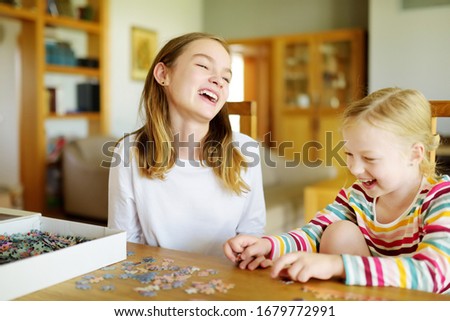 Cute young girls playing puzzles at home. Children connecting jigsaw puzzle pieces in a living room table. Kids assembling a jigsaw puzzle. Fun family leisure. Stay at home activity for kids.