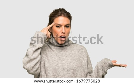Blonde woman with turtleneck making the gesture of madness putting finger on the head over isolated grey background