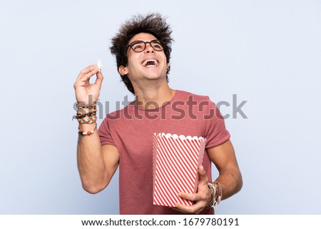 Young caucasian man over isolated background with 3d glasses and holding a big bucket of popcorns
