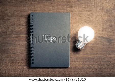 Black notebook with text TIPS and glowing light bulb on wood background Royalty-Free Stock Photo #1679781310