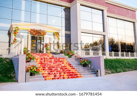 Autumn decoration of the facade of the building. Staircase with bouquets of yellow leaves and a red walkway.