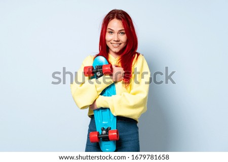Teenager red hair girl isolated on blue background with a skate with happy expression