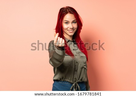 Teenager red hair girl isolated on pink background making money gesture