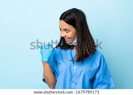 Surgeon woman over isolated blue background pointing to the side to present a product