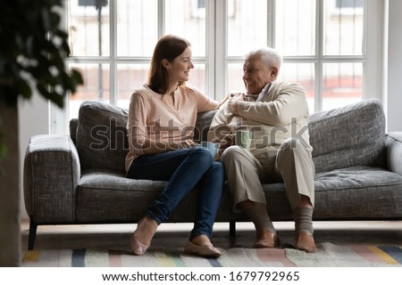 In cozy living room caring adult daughter drink tea with old dad family enjoy talk sit on comfy couch. Caregiver and patient care, attention, love, strong connection with older relative person concept Royalty-Free Stock Photo #1679792965