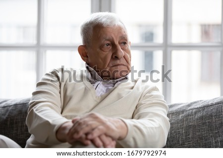 Pensive old man resting at home sitting on couch in living room alone. Aged 80s baby boomer older generation male lost in sad thoughts feels lonely, recollect life moments has nostalgic mood concept Royalty-Free Stock Photo #1679792974