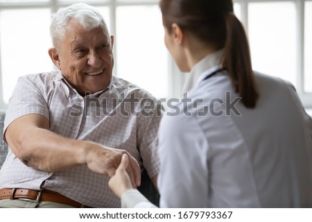 Nurse in uniform talking during day visit to old patient. Caring caregiver hold hand of 80s man people having pleasant conversation, satisfied grandfather receiving support and care from carer concept Royalty-Free Stock Photo #1679793367
