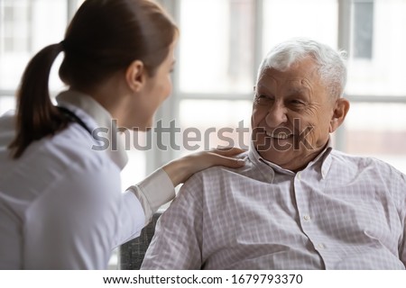 Caring geriatric nurse in white coat cares for grey-haired elderly man in nursing home, listen him relieve solitude, provide support help during visit at home. Homecare eldercare caregiving concept Royalty-Free Stock Photo #1679793370