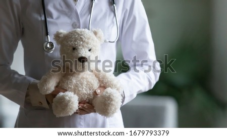 Close up image female paediatrician in white coat holding pretty stuffed toy bear, private clinic professional care about the smallest patients, pediatrics branch of medicine. Concept of healthcare Royalty-Free Stock Photo #1679793379