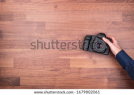Professional photographer is preparing for photo shoot and take DSLR photo camera from wooden table. Photographer design element ideal for background.