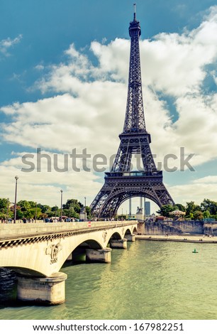 Eiffel tower in Paris, France. Famous Eiffel tower and old Jena Bridge at Seine river in summer. Vintage photo of World landmark on sky background. Vertical view of famous Tour. Travel, tourism theme