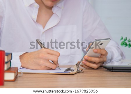closeup of student at the desk with mobile phone and typing