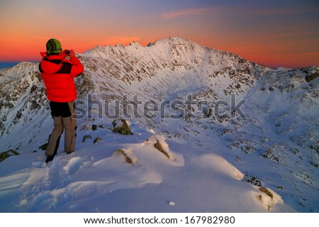 Sunset landscape with climber taking pictures of snowy mountains
