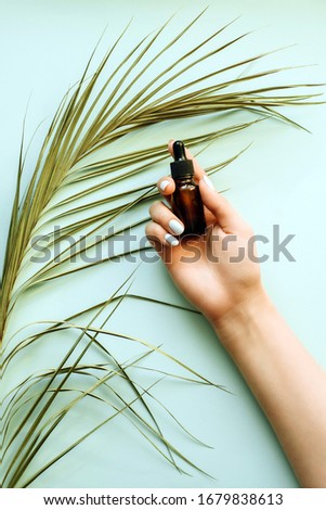 Moisturizing serum on the background of a palm leaf in a girls hand. Blue pastel background. Template for advertising, blog. The concept of skin care