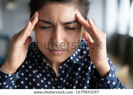 Close up exhausted Indian girl touching forehead, unhappy upset girl suffering from strong headache or migraine, overworked tired young female feeling pain in head, health problem concept Royalty-Free Stock Photo #1679841097