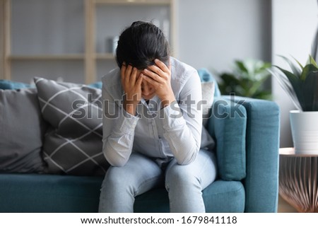 Unhappy depressed Indian woman holding head in hands, sitting alone on couch at home, stressed young female worried about bad relationship, break up, thinking about problems, feeling lonely Royalty-Free Stock Photo #1679841118