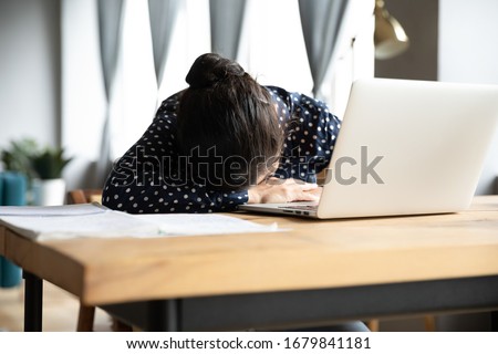 Tired Indian woman sleeping, sitting at desk with laptop, overworked girl lying on table, insomnia, health problem, exhausted young female unmotivated student falling asleep, feeling boredom Royalty-Free Stock Photo #1679841181