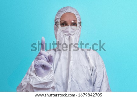 woman in overalls, protective glasses, mask and white gloves raises a finger as a sign of attention. The concept of public health